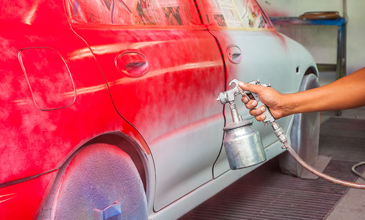 Auto body technician using airbrush on car